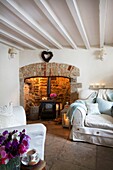 Wood burning stove and slip covered three-piece-suite in whitewashed living room of Corfe Castle cottage, Dorset, England, UK