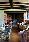 Woodburner on brick fireplace with Moroccan coffee table in beamed living room in Sandhurst cottage, Kent, England, UK