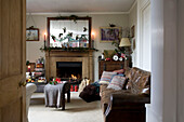 Christmas decorations hang on mirror above lit fire in living room of Tenterden home, Kent, England, UK