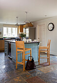 Hellblaue Kücheninsel mit hölzernen Barhockern und Tasche in einer Küche mit Schieferfußboden in einem Haus in Smarden, Kent, England