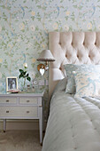 Buttoned headboard with hear on lamp in floral patterned bedroom of Kent home England UK