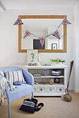 American bunting hangs on mirror above sideboard with light blue painted wicker chair in Dartmouth home, Devon, UK
