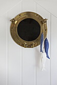 Brass porthole window with fish on white panelled wall in Dartmouth home, Devon, UK