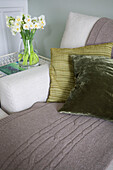 Green cushions with cut daffodils and brown woollen throw on sofa in Deal home Kent England UK