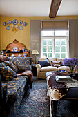 Cremefarbene und blau gemusterte Sofas mit Ponyskin auf Ottomane im Wohnzimmer eines Bauernhauses in Etchingham, East Sussex, England, UK