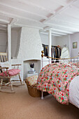 Floral quilt on double bed with rocking chair and whitewashed fireplace in High Halden farmhouse Kent England UK