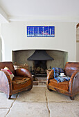 Pair of brown leather armchairs at fireplace with artwork in Bishops Sutton home Alresford Hampshire England UK