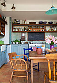 Painted chair with wooden table and open shelving in kitchen of Hackney home London England UK