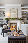 Gestreiftes Sofa und Ottomane mit beleuchtetem Holzofen und Weihnachtsdekoration in einem Londoner Haus UK