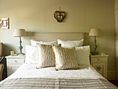 Matching lamps on bedside cabinets with cushions on bed in Kensington home London England UK
