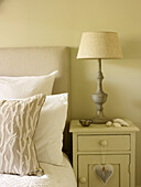 Lamp on bedside cupboard with padded headboard and cushions in Kensington home London England UK