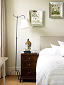 Silver framed artwork above wooden bedside cabinet with lamp in Kensington home London England UK