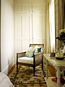 Wicker chair with patterned rug and built-in wardrobe in Kensington home London England UK