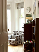 View through doorway with upholstered armchair and wooden storage in London home England UK
