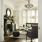 Grey armchair at fireplace with wicker stool and chandelier in living room of London home England UK