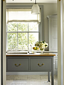 Cut flowers on grey kitchen island with sash window in kitchen of East Sussex country house England UK