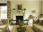 Crocus on checked ottoman with sofas and marble fireplace in living room of East Sussex country house England UK