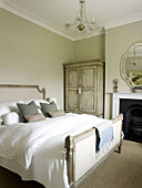 Grey cushions on double bed with wardrobe and original fireplace in East Sussex country house England UK