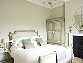 Grey cushions on double bed with restored wardrobe in East Sussex country house England UK