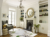 Runder Spiegel über dem Kamin mit Bücherregalen im Wohnzimmer mit grauem Sessel North London Stadthaus England UK