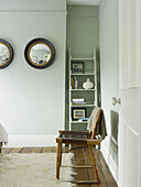 Wicker chair with bookshelf and convex mirrors in light blue North London townhouse England UK