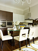 White leather armchairs at glass table in dark wooden kitchen of Little Venice townhouse London England UK