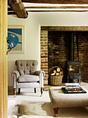Buttoned armchair with log basket at fireside in timber-framed West Sussex farmhouse, England, UK