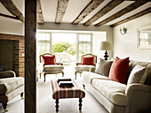Red cushions on seating with striped ottoman in timber-framed West Sussex farmhouse, England, UK