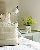Light green cushions with cut flowers and lamp on bedside in West Sussex farmhouse, England, UK