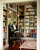 Ladder and bookcases with piano in library with polished parquet floor in London townhouse apartment, UK