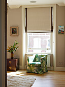 Upholstered armchair at sunlit window in London townhouse apartment, UK
