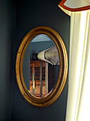 Wooden cabinet reflected in oval mirror in London townhouse, UK