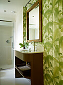 Wood framed mirror above wash stand with leaf patterned wallpaper in London townhouse, UK