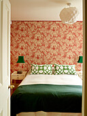 View through doorway to bedroom with green accent colours, vintage wallpaper and paper shade, London townhouse, UK