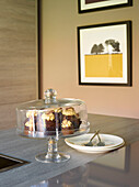 Chocolate cupcakes and plates on worktop with framed artwork in Manchester home, England, UK