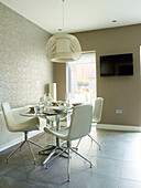 Pendant shade above dining table with cream chairs and wall-mounted TV in Manchester home, England, UK