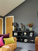 Black side shelf set against grey wall with brown leather sofas in Manchester home, England, UK