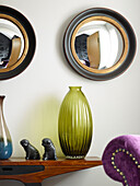 Convex mirrors above coloured glass vase on wooden side table in Manchester home, England, UK