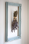 Lavender flowers tied in a bunch upside down drying in a pastel blue frame against a white wall