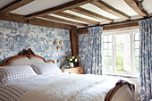 Antique bed under low beamed ceiling in room with toile wallpaper and open window, timber framed cottage, Kent England, UK