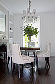White dining chairs at table with leaf arrangement under chandelier in London home UK