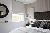 Striped cushions and circular mirror in bedroom of London home UK