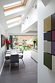 Dining table below skylights with artwork in open plan kitchen extension of contemporary London home, England, UK