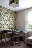 Office chair at desk in room with co-ordinating wallpaper and lampshade in contemporary London home, England, UK