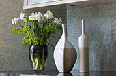 Vase mit Narzissen und Töpferwaren mit gemusterter Tapete in einem Haus in Cambridgeshire UK