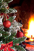 Red baubles on artificial tree at fireside in Kent home England UK