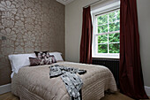 Cream quilted bedcover with floral patterned wallpaper on bed at window of Sussex home UK