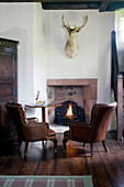 Brown leather armchairs and hunting trophy with lit fire in Scottish home UK