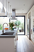 Pendant lights and cut tulips on kitchen island in extension of London home, UK