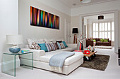 Coffee table with caster wheels and white sofa below modern art in double room of contemporary London home, UK